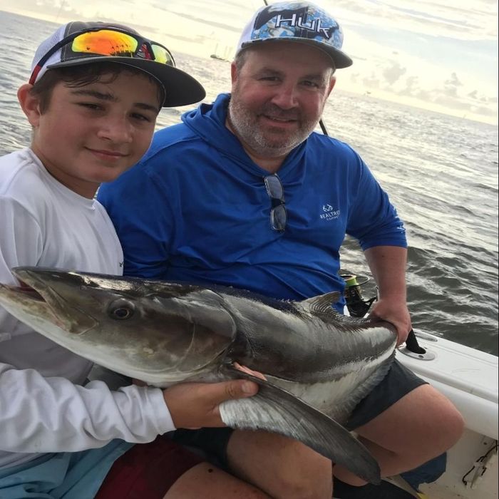 father and son sitting on the side of a boat holding a huge fish