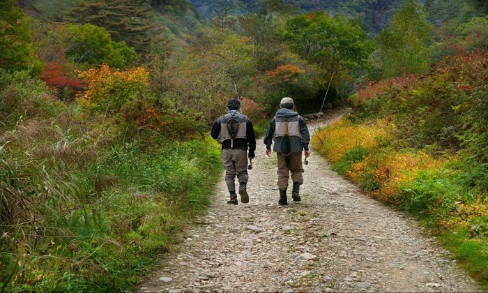 two men with fishing gear walking along the rocky road