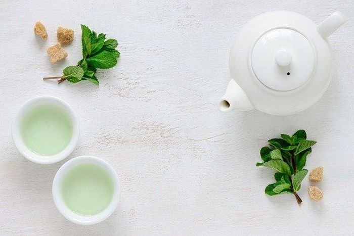 Two cups of green tea and a white tea pot 