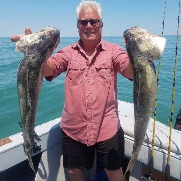 an old man holding giant fish on his hands while standing on a boat