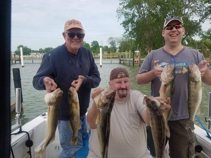 2 young adult and one old man sitting on a boat and holding fish on their hands