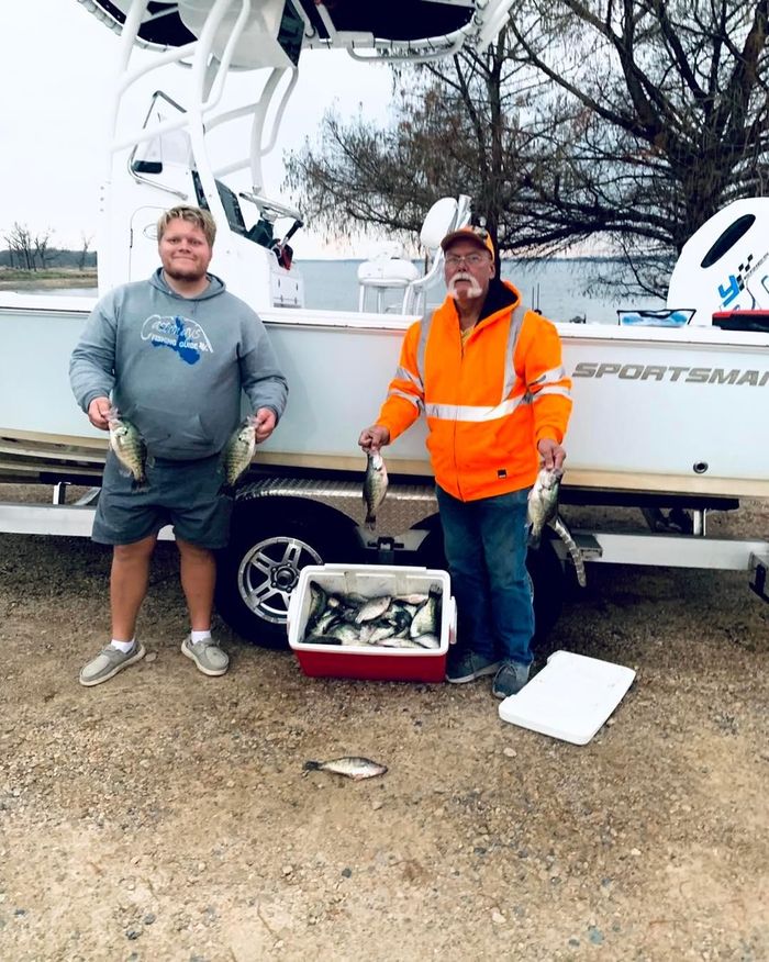 2 men standing beside a white boat holding fish on their hands