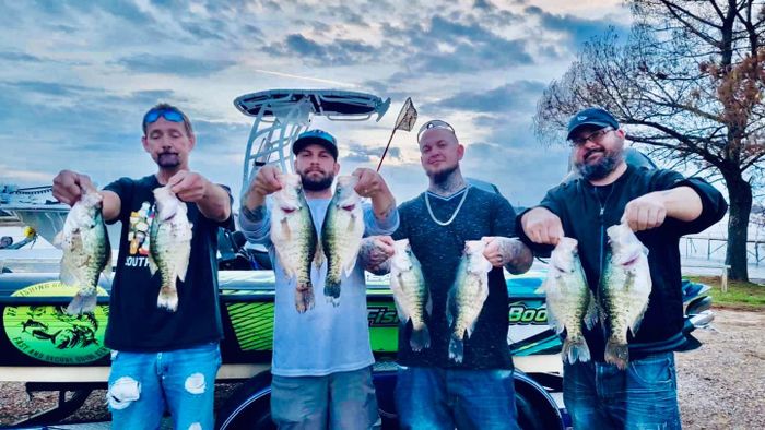 4 men holding fish on their hands with a boat behind them