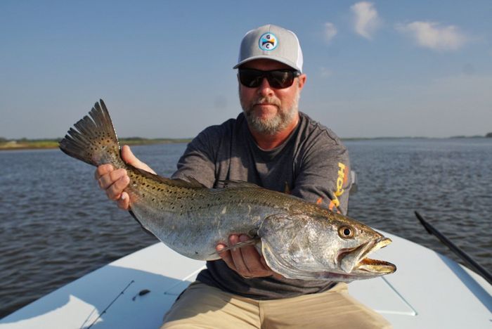 man sitting on a white boat holding a giant trout