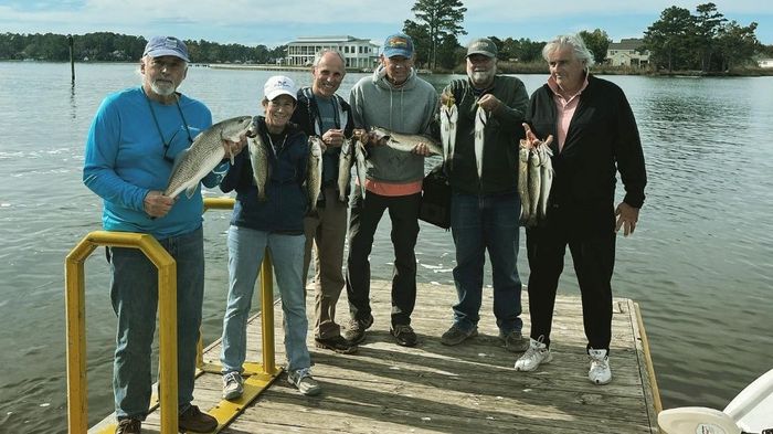 group of people holding different kinds of fish standing on a wooden dock