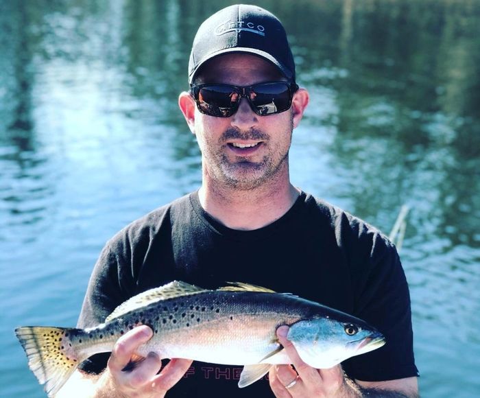 man on a black cap and shades holding a medium-sized fish