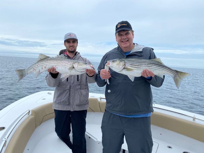 2 men standing on a boat and holding striped bass