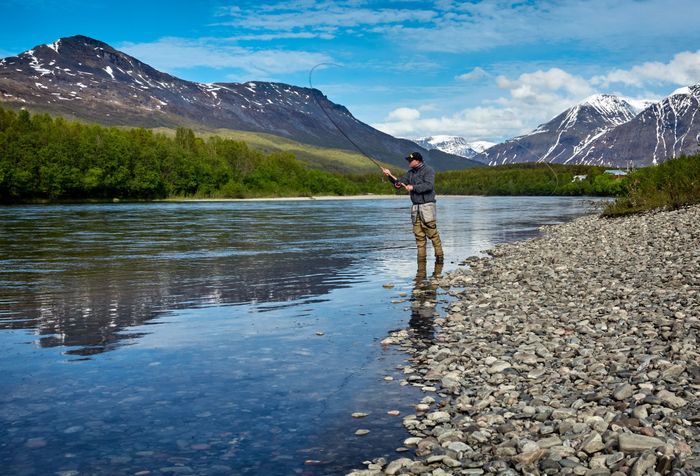 Man fishing on the shallow part of the river with the view of the mountains