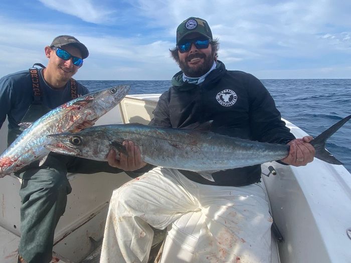 2 men sitting on a charter boat and holding fish 