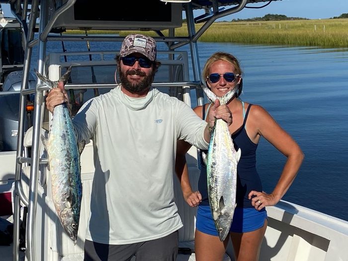 man and a woman standing on a boat with the man holding 2 fish on his hands