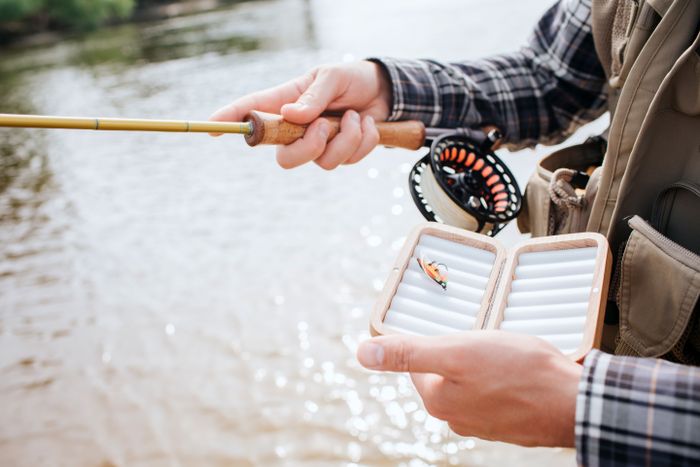 cut-view-man-standing-water-holding-spinning-with-reel-one-hand-box-with-one-artificial-silicone-fishing-lure-with-other-one-guy-wears-vest.jpg