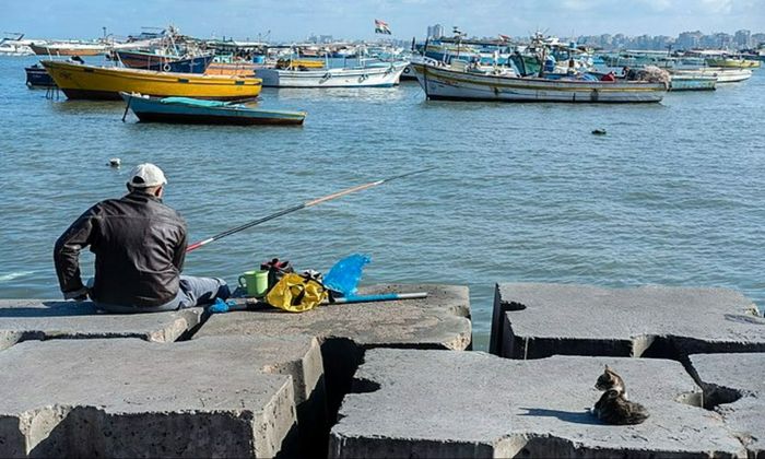man sitting and fishing at the edge of the water body