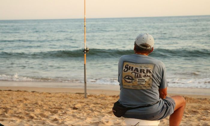 man looking at his fishing rod near the sea