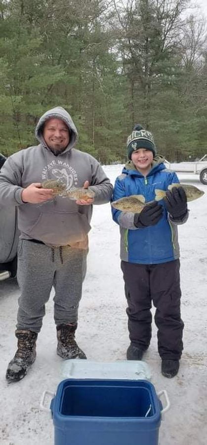 man and a kid standing on snow and holding fish 