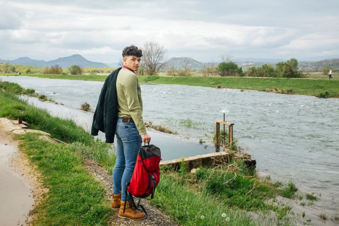 young-hiker-standing-near-flowing-river-with-holding-backpack-looking-camera.jpg