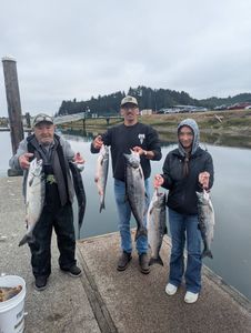 Three anglers displaying their catch of Coho salmon at a marina dock in Roseburg OR