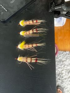 Four colorful fishing flies with yellow, brown, and red feathers arranged on dark surface in Tavernier FL