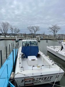 White fishing boat with blue cabin docked at Port Clinton Ohio marina on overcast day