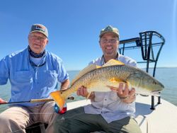 Two anglers displaying a caught redfish on a fishing boat