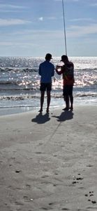 Two anglers fishing from the beach at New Smyrna Beach FL with fishing rod extended toward ocean waves