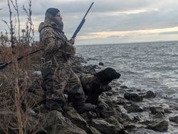 Hunter with black dog sitting on rocky shoreline near water in Detroit MI