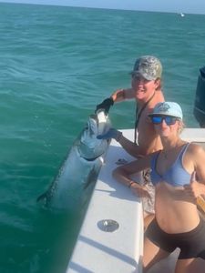 Large tarpon jumping out of turquoise water next to fishing boat in Holmes Beach FL
