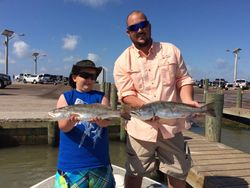 Father and son with shiny speckled trout at dock.