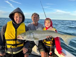 A group of 4 people on a fishing cruise in MA, catching a striped bass