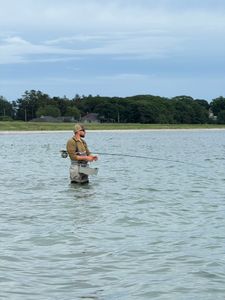 Fishing guide wading in calm water near wooded shoreline in South Portland Maine