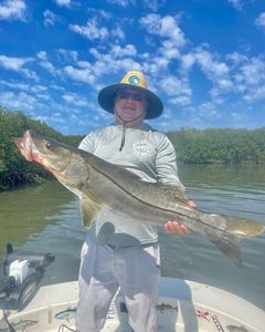 An angler holds a large snook fish against a backdrop of the Florida coast.