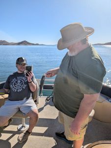 A day spent on the lake, surrounded by breathtaking scenery and the peaceful tranquility of nature. The two individuals, one capturing the moment on a smartphone and the other readying their fishing gear, appear to be fully immersed in the serene outdoor experience.