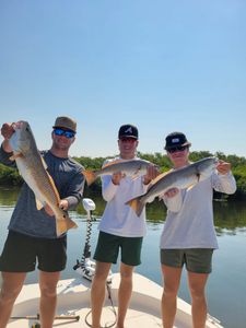Two anglers holding three large redfish they caught while fishing in Florida
