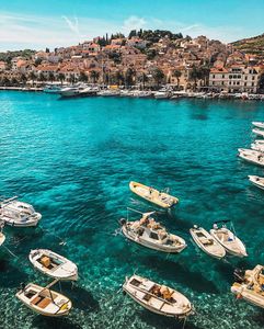 Fishing boats anchored in crystal clear turquoise waters near Mediterranean coastal town with red tile roofs
