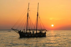 Traditional sailing vessel with two masts silhouetted against orange sunset on calm waters in Destin FL