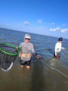 Wading fishing scene in Matagorda TX with fishing net and rod in shallow coastal waters