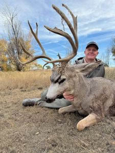 Hunter with harvested mule deer buck displaying large antler rack in Lamar Colorado grassland