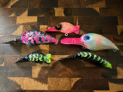 Five colorful fishing lures with bright pink, green, and iridescent finishes displayed on wooden cutting board in Centralia WA