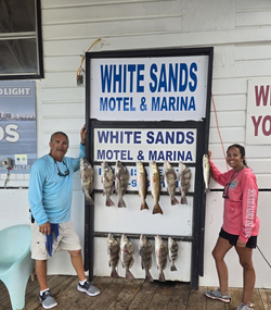 Two anglers holding their catch of 12 black drum fish on the shore at South Padre Island
