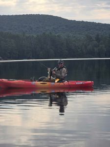 Angler fishing from red kayak on calm lake in North River NY with forested hills in background