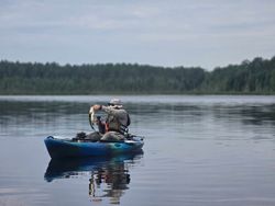 Angler in blue kayak fishing on calm lake in North River NY surrounded by forested shoreline