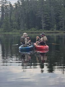 Two anglers in kayaks fishing on calm lake waters in North River NY surrounded by dense forest