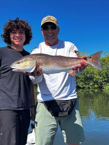 Two anglers displaying a caught redfish on a boat in Hudson FL waters with mangroves in background