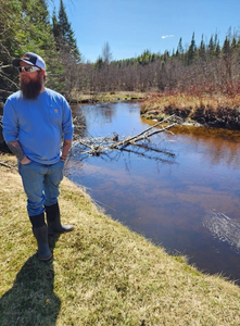 Person standing beside calm stream with fallen logs in Owls Head NY wilderness area