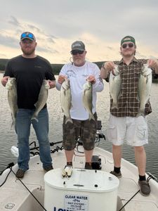 Three anglers displaying striped bass catch on fishing boat in Mannford OK
