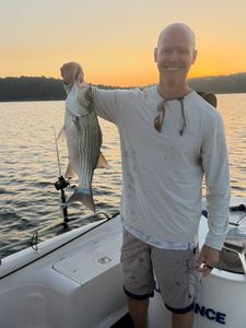 Angler holding striped bass on boat at sunset in Mannford OK