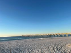 Wooden fishing pier extending into blue ocean waters with white sandy beach at Fort Walton Beach FL