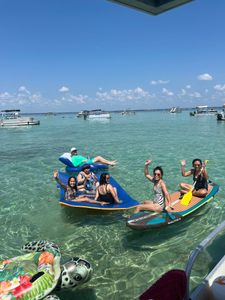 Group enjoying water activities on inflatable rafts and paddleboard in clear turquoise waters near Fort Walton Beach FL with boats anchored in background