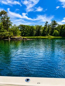 Calm lake waters surrounded by lush green forest from fishing boat deck in Wells Harbor ME