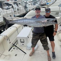 Two anglers holding large wahoo fish on boat deck at marina in New York City