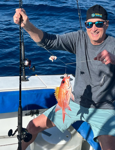 Angler displaying freshly caught colorful fish on fishing boat deck with rod and reel equipment visible